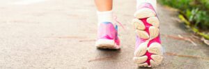 close up of two feet walking on cement wearing hot pink and white athletic shoes