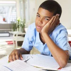 young boy leaning on his hand, frustrated, with homework beneath him